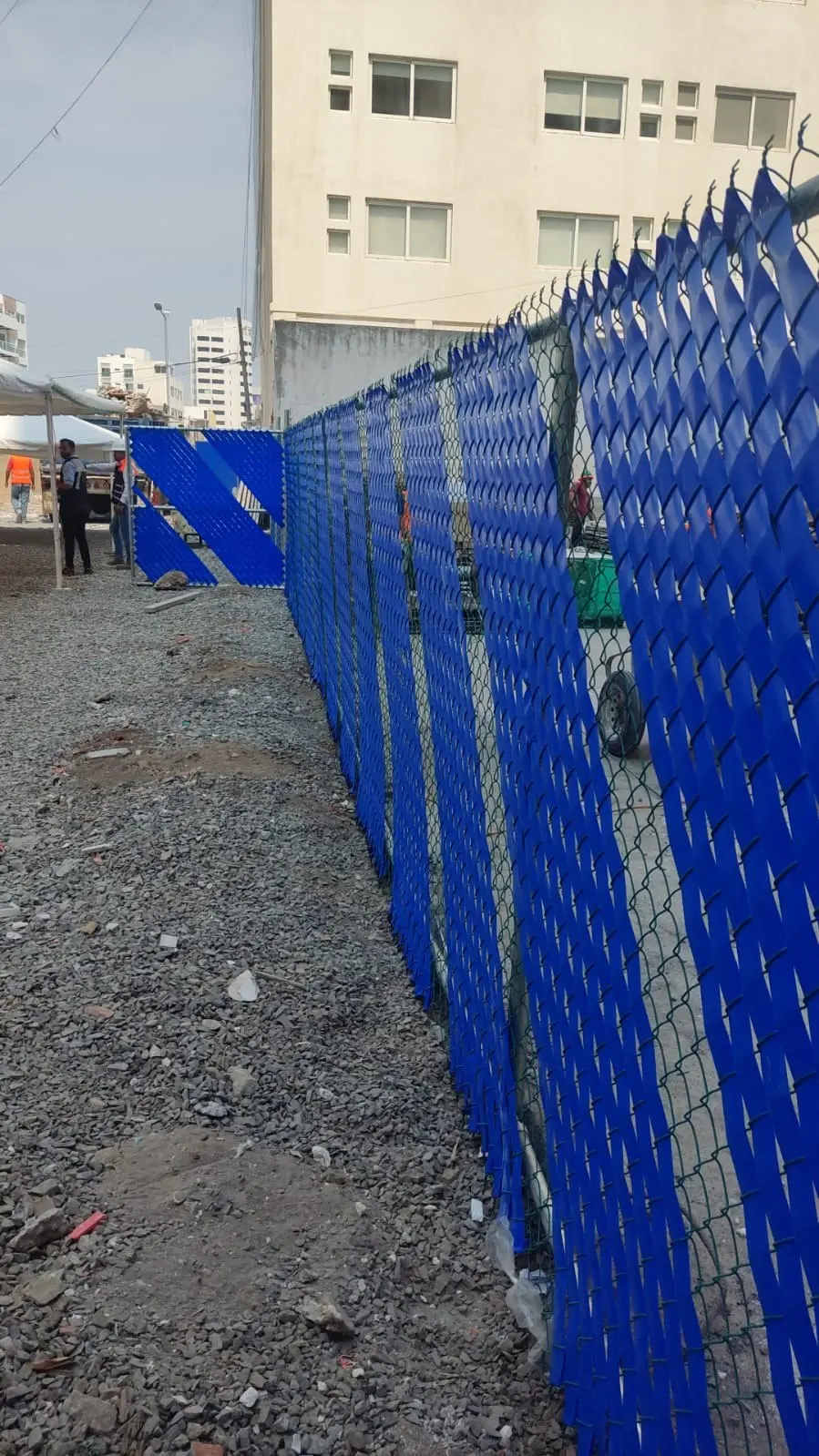 Malla ciclónica con cinta de privacidad azul en diagonal a lo largo de un terreno en obra