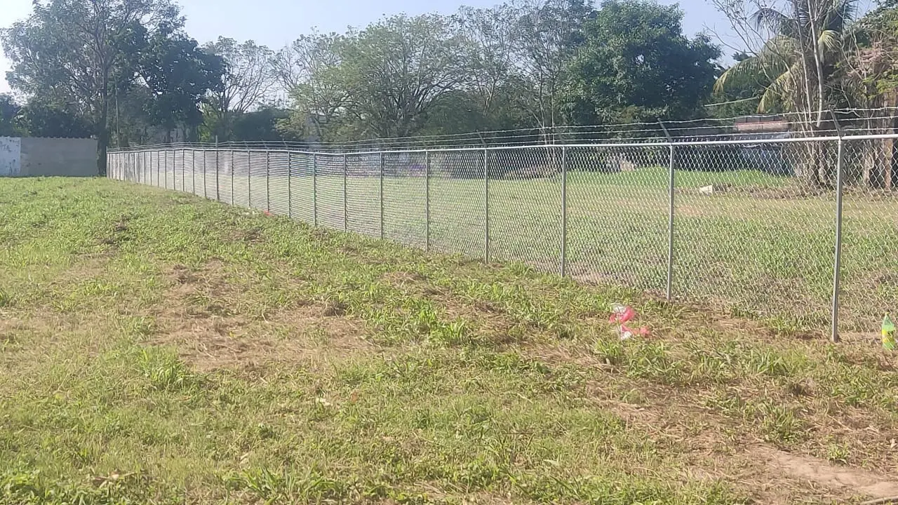 Cerca larga de malla ciclónica galvanizada alrededor de un terreno grande con pasto y árboles