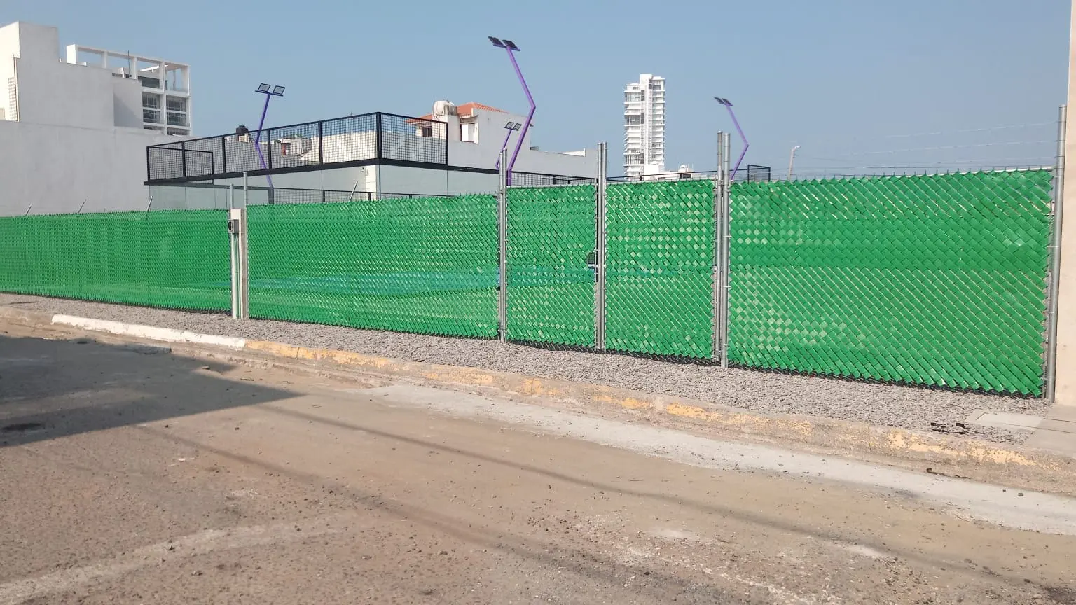 Cerca de malla ciclónica con cinta de privacidad verde a lo largo de una calle