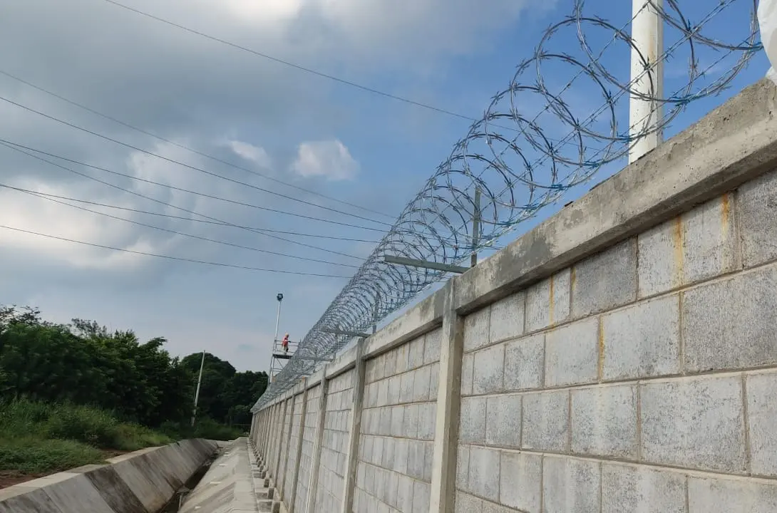 Concertina galvanizada instalada sobre una barda larga de block junto a un canal