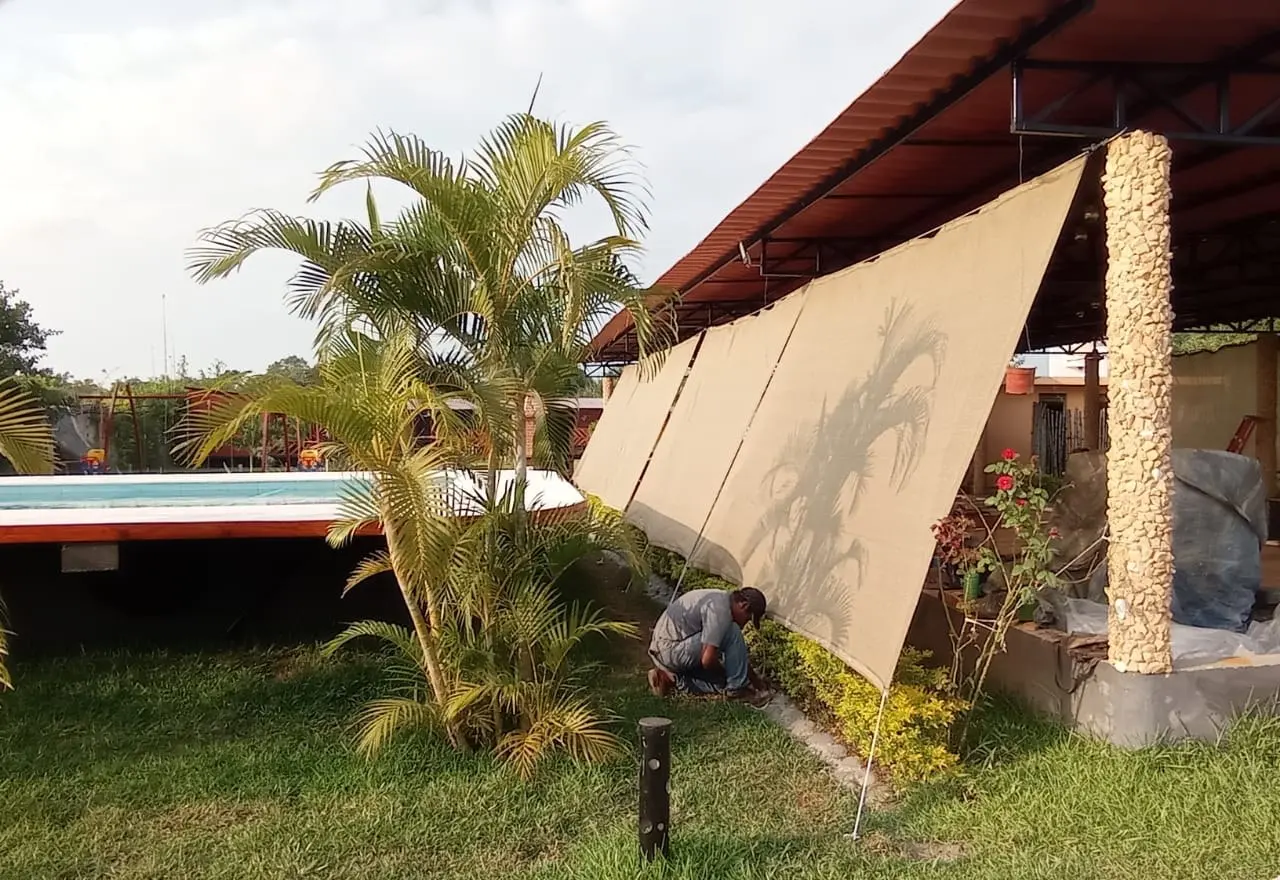 Instalador colocando malla sombra al 95% en un jardín con alberca