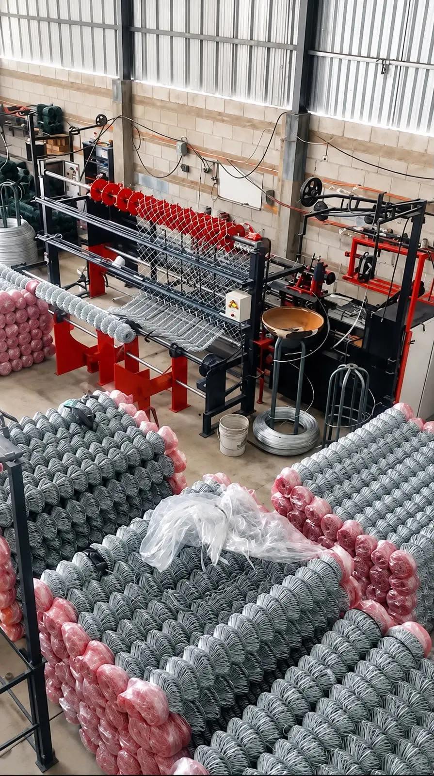 Máquinas tejedoras y rollos de malla ciclónica galvanizada en la planta de Cercas y Techos