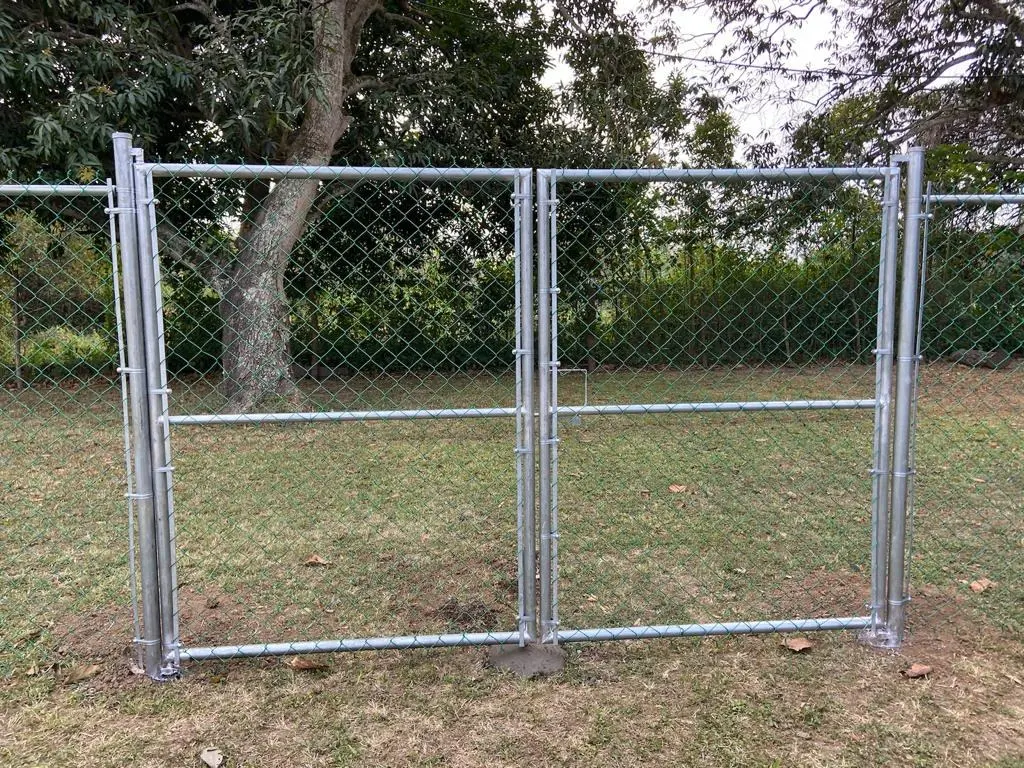 Puerta doble de malla ciclónica galvanizada recién instalada en la entrada de un terreno con árboles